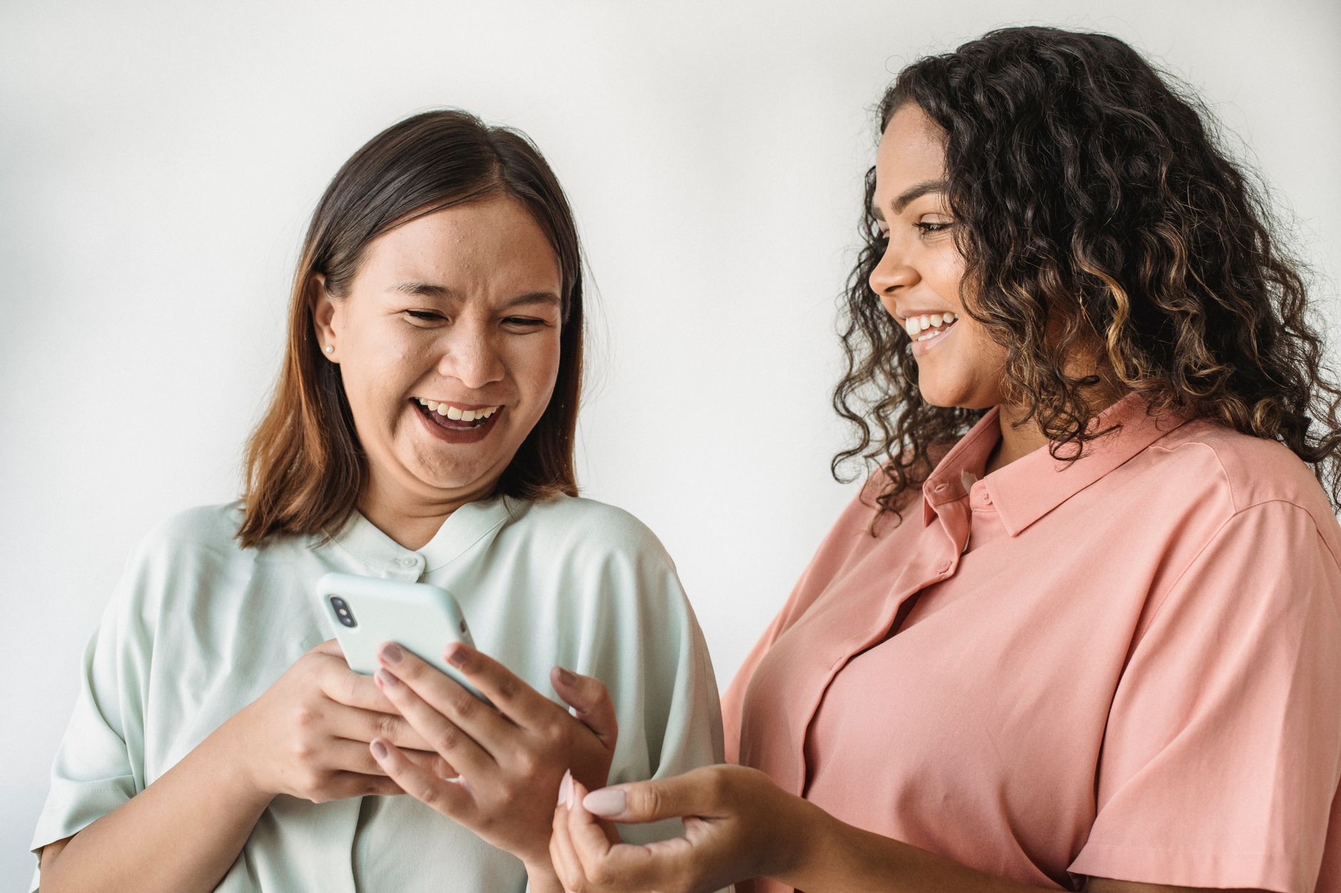 Two diverse women happily looking at and sharing something on a smartphone indoors.