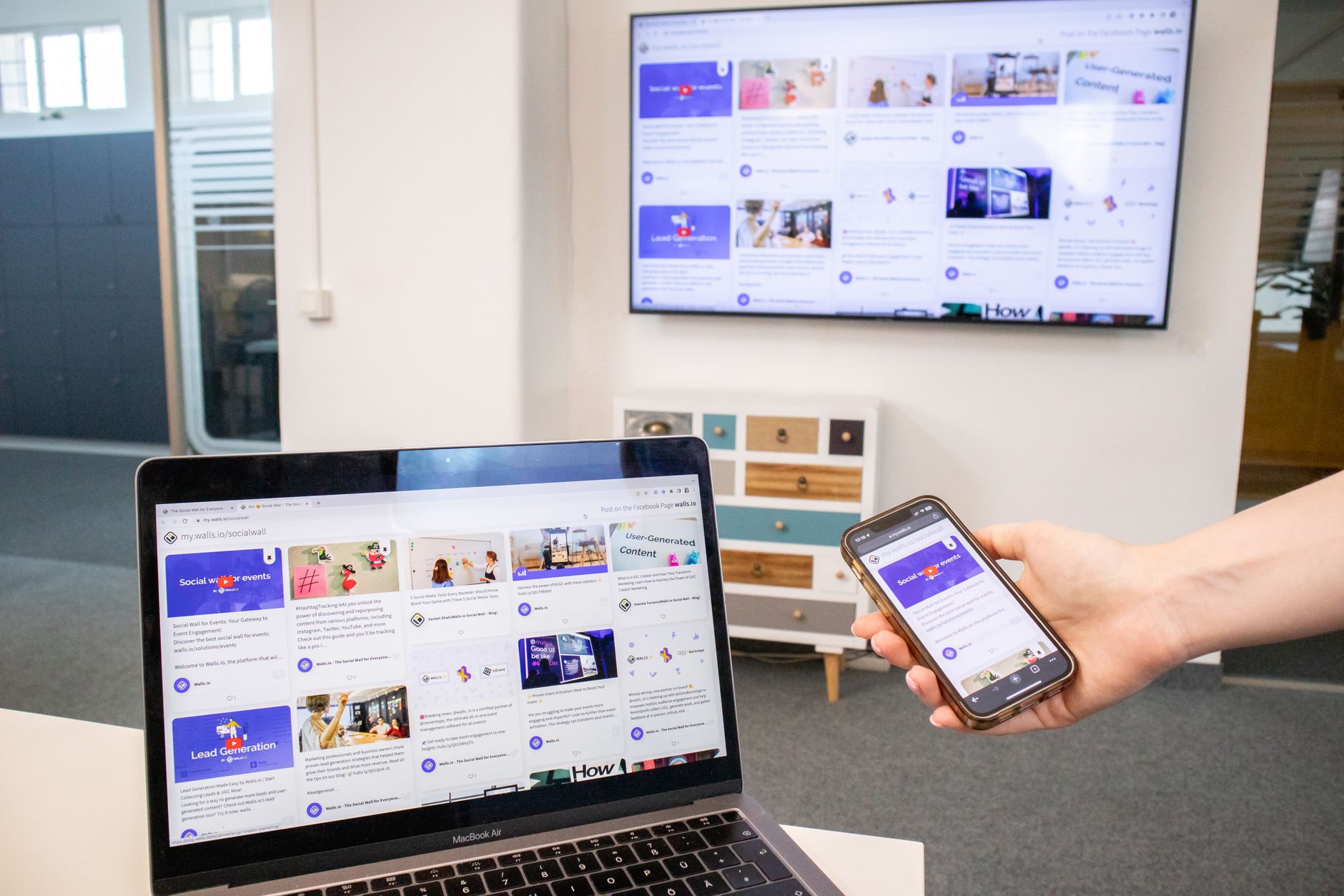 Digital devices including a laptop, phone, and TV in a modern office setting showing content synchronization.