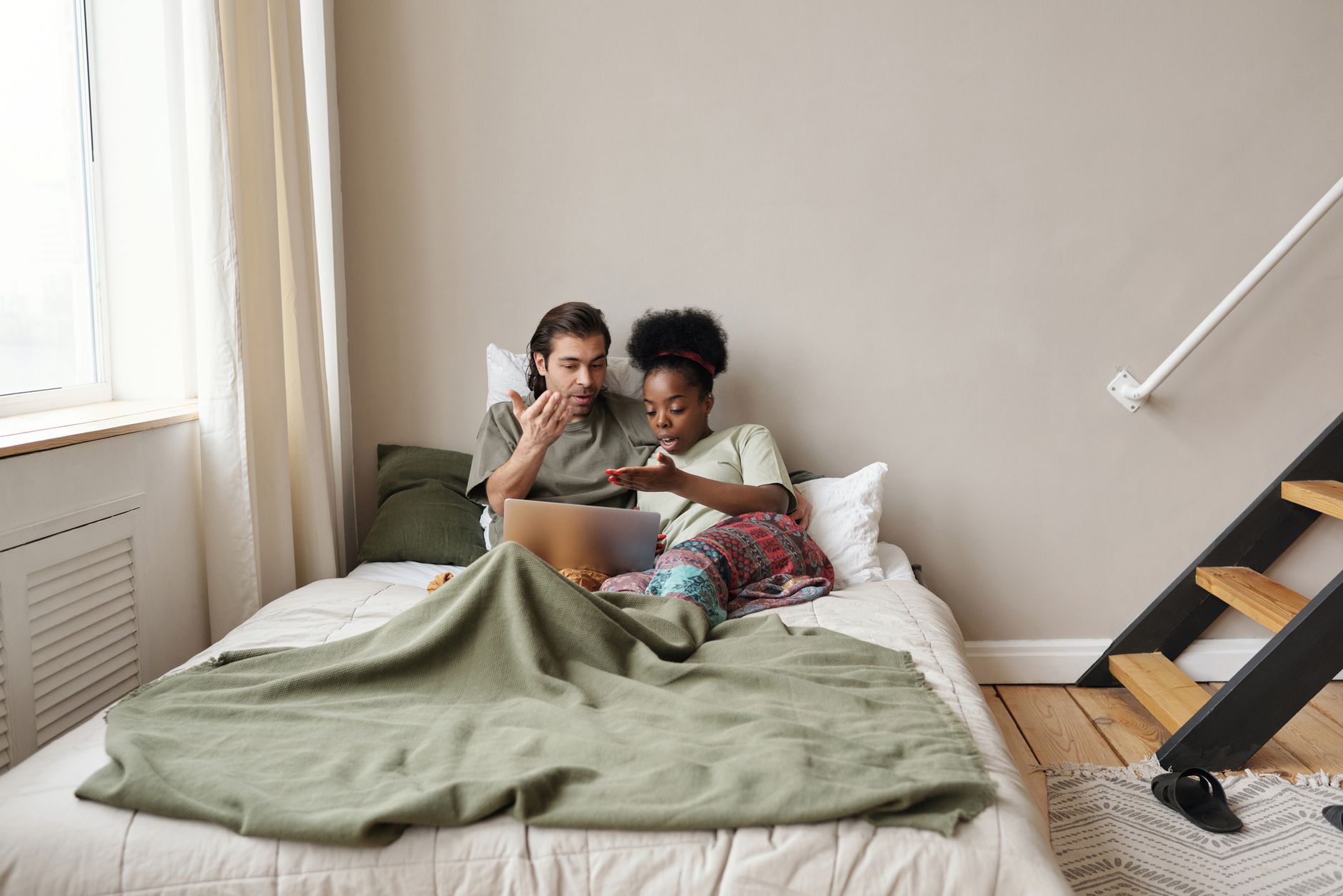 Multiracial couple watching content and relaxing on bed, sharing moments together.