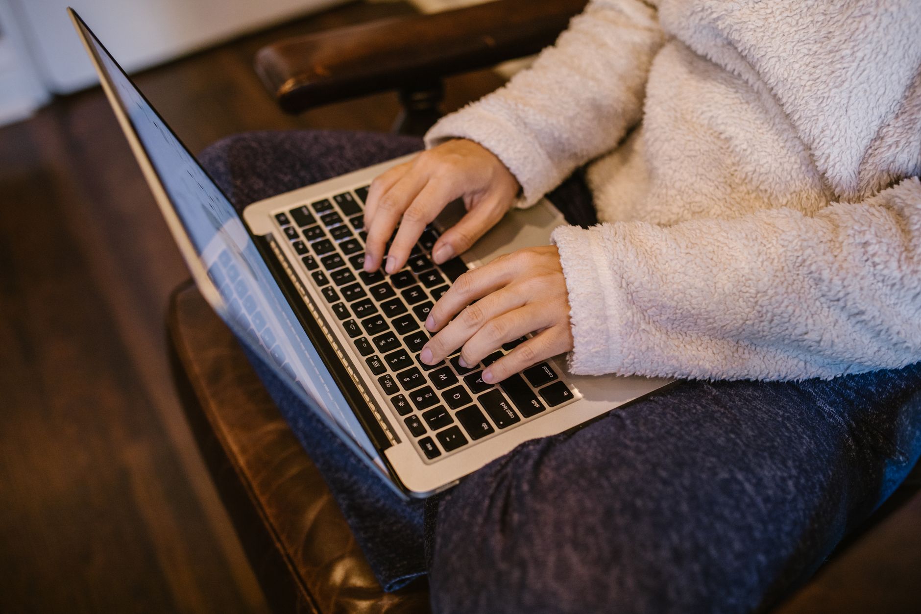 Close-up of hands typing on a laptop, wearing a warm fleece sweater, depicting home learning.