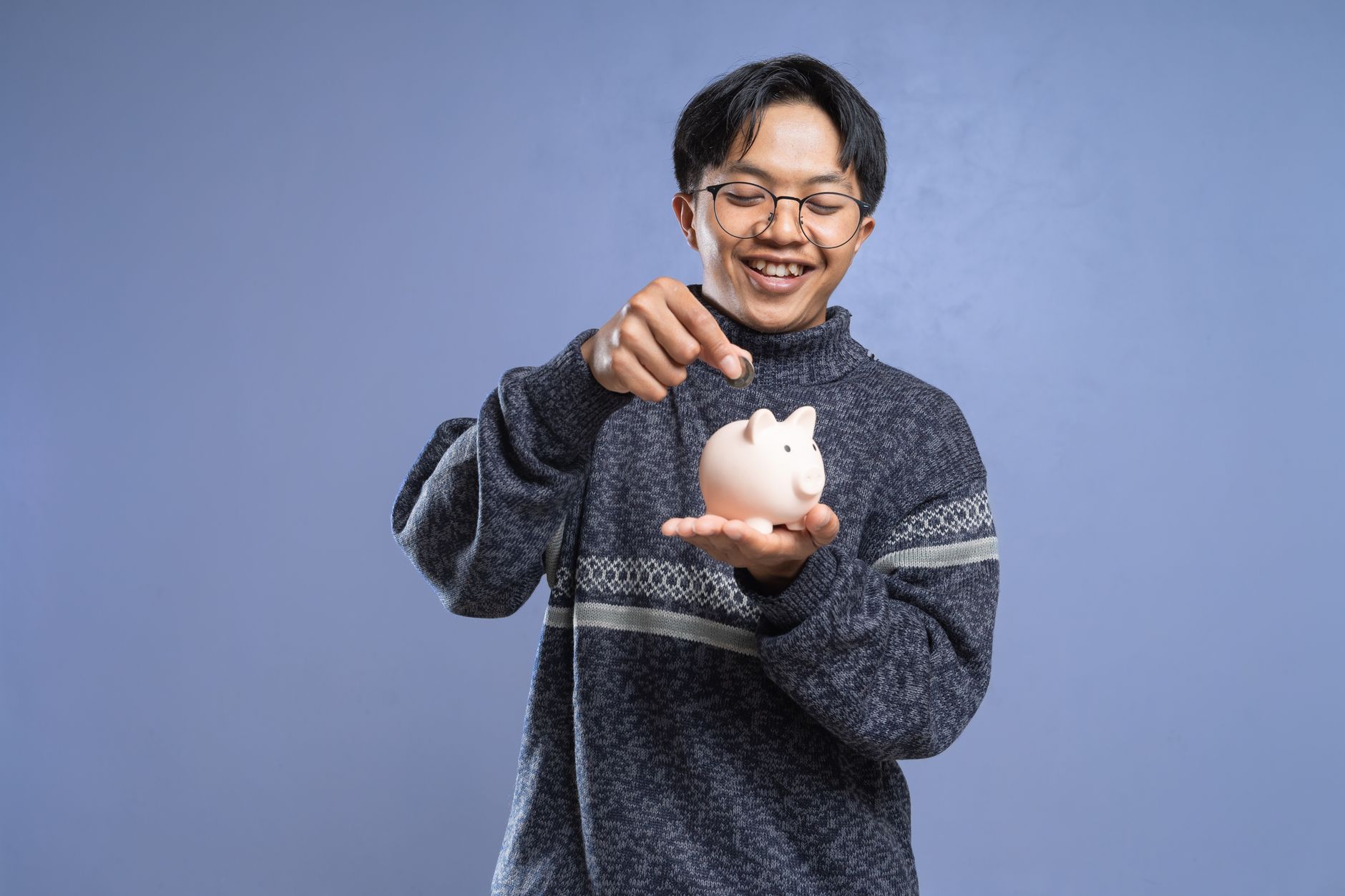 Smiling man holding a piggy bank and inserting a coin, representing savings and financial planning.